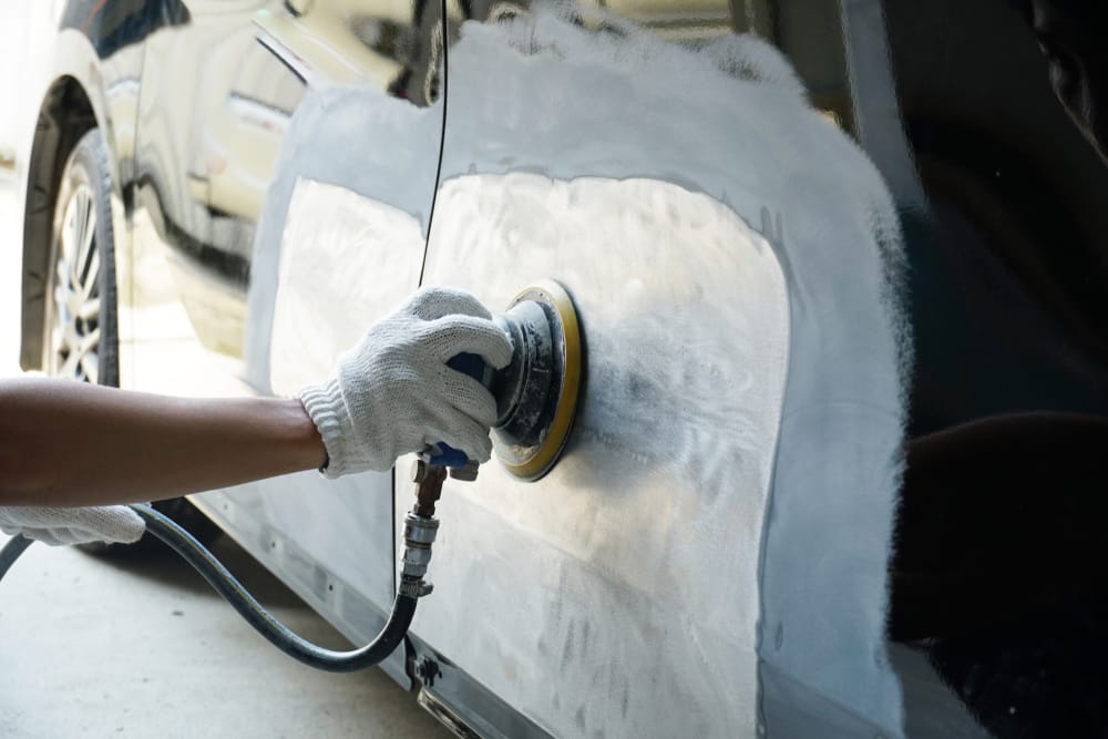 Technician sanding body filler on a prepared panel before paint